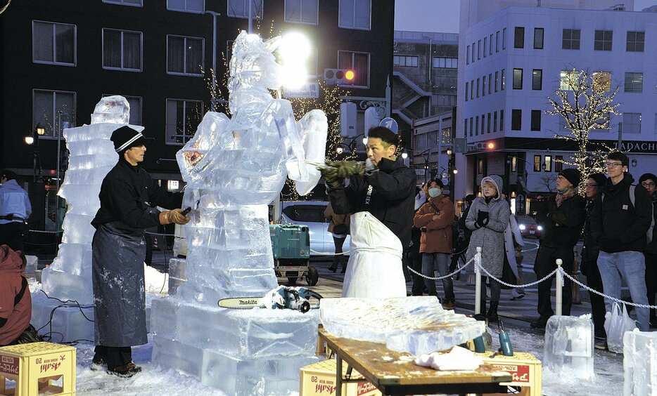 美しい氷の芸術作品を削り出す職人と制作に見入る観光客ら