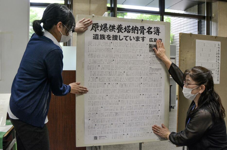 広島市役所で、原爆死没者の氏名や年齢を記載したポスターを掲示する市職員＝14日午前