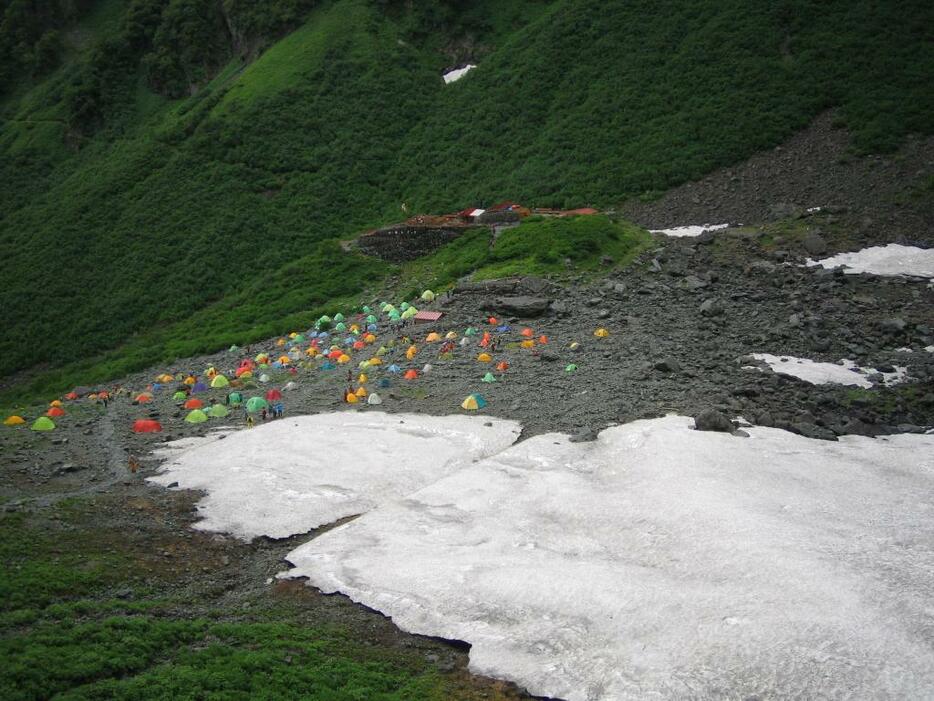 [写真]残雪の近くのテント場がにぎわう夏の涸沢（からさわ）