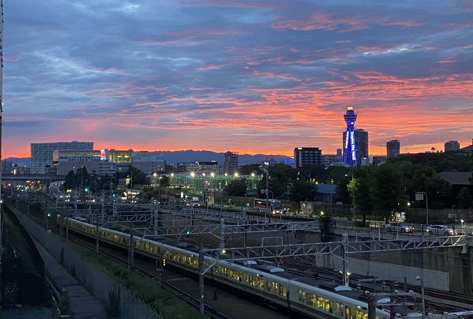 20日の大阪市内は湿った空気の影響で雨が降るなどしていたが、夕方には真っ赤に染まる夕焼けが見られ、歩道橋から多くの人が通天閣方面を撮影していた＝20日午後6時45分ごろ、大阪市阿倍野区で