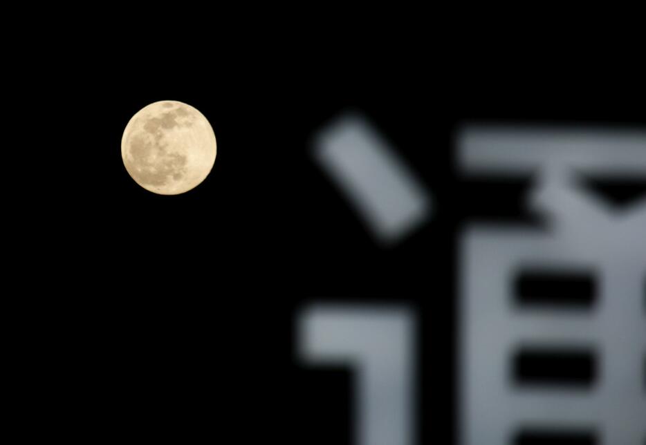 ［写真］大阪市浪速区の1階入り口付近からも大きな月を見ることができ、道行く人がカメラ撮影を楽しんでいた＝16日午後7時すぎ、大阪市浪速区で