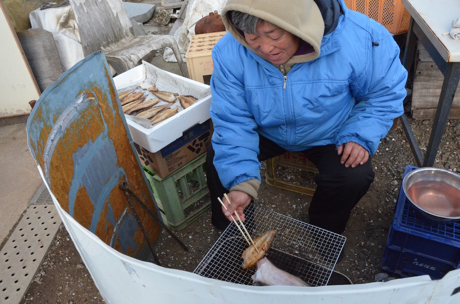 青い小屋の前で、シタビラメを焼く佐藤さん