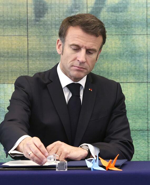 机の上に置かれた折り鶴のレプリカを手にするフランスのマクロン大統領＝19日、広島市の原爆資料館