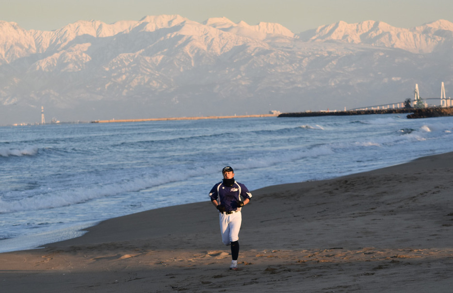 全体練習後、夕焼けに染まる富山湾越しの立山連峰を背に黙々と走り込みを続ける青野拓海投手＝富山県氷見市の島尾海岸で２０２３年２月２７日、青山郁子撮影