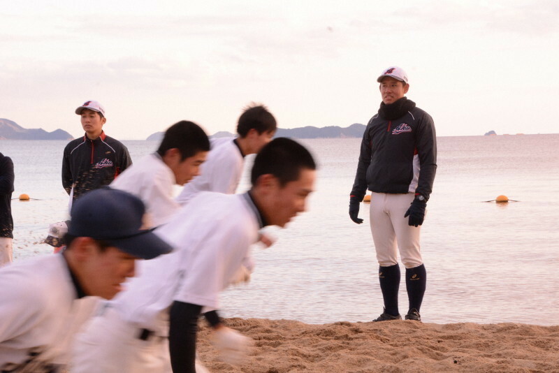 砂浜でダッシュする選手たちを見つめる赤穂高校の頓田郷平監督（右）＝兵庫県赤穂市で2020年2月1日午後4時40分、福田隆撮影