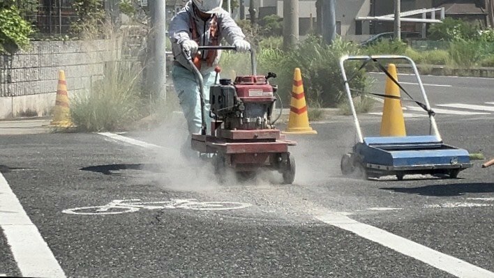 抹消機で自転車横断帯を消す作業員（福山市水呑町）