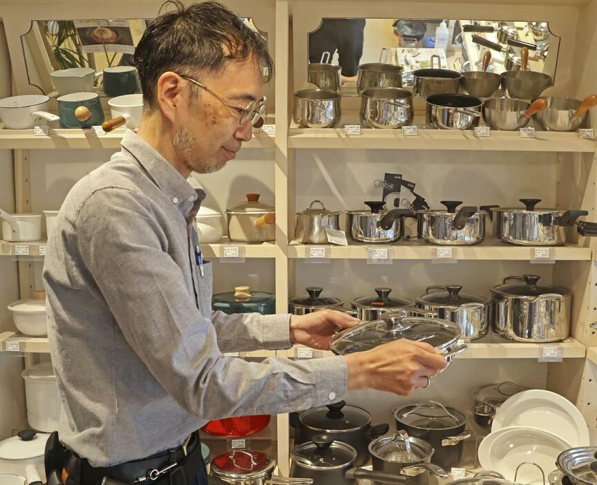 商品の鍋を手に取る創業465年の老舗調理器具専門店「鍋屋」店主の水野文雄さん＝2024年6月、名古屋市