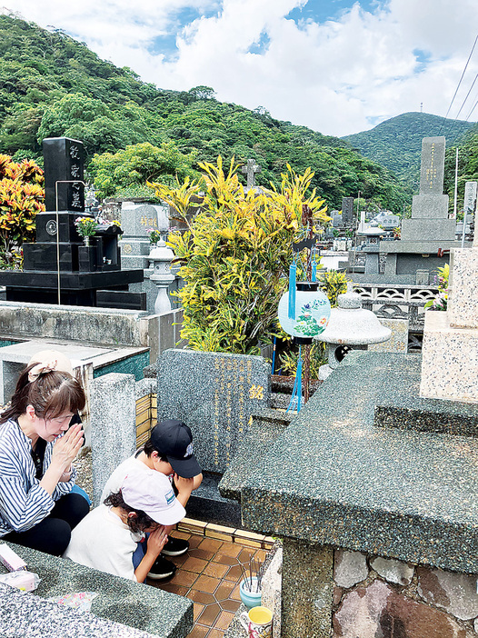 ちょうちんをつるし、墓前で手を合わせる家族＝16日、鹿児島県奄美市名瀬の永田墓地