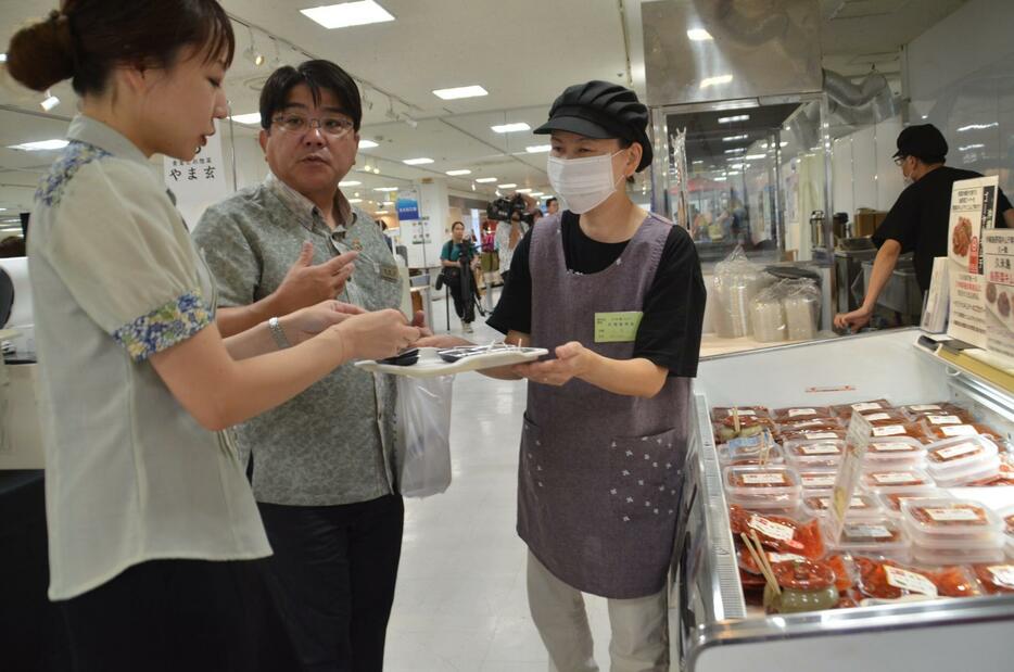 ゴーヤーや島らっきょうなど島野菜のキムチの試食を楽しむ久米島フェアの来場者＝30日、那覇市のデパートリウボウ