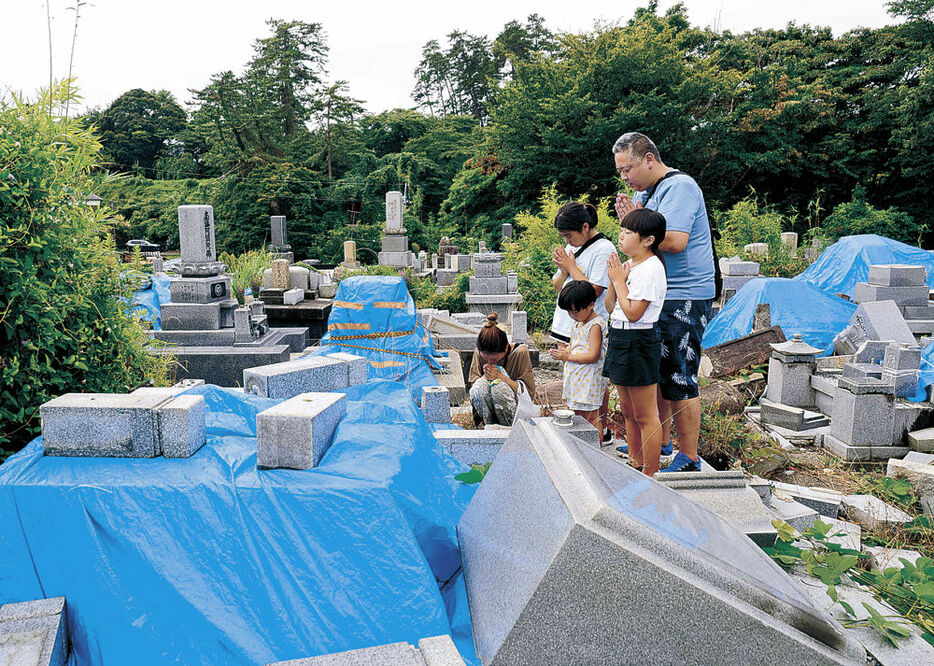 修繕が間に合わず、ブルーシートで覆われた墓に手を合わせる家族連れ＝輪島市河井町