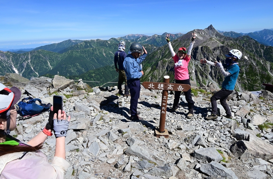 槍ケ岳を背景に北穂高岳の頂上で写真撮影する登山者