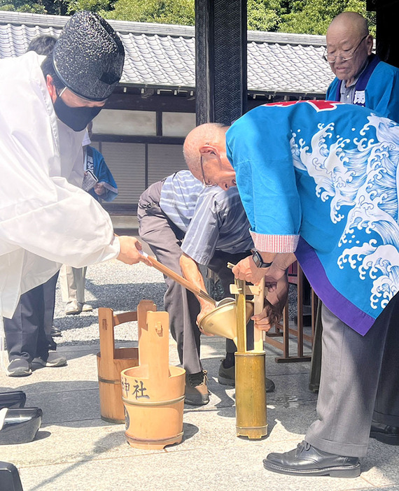 持参した竹筒に雷電沼の御神水を頂く脚折雨乞行事保存会の横沢運治会長（右）＝3日午前、群馬県板倉町の板倉雷電神社