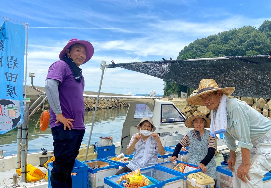 黒島の波止場で岩田さん（左端）が並べた商品を見る住民