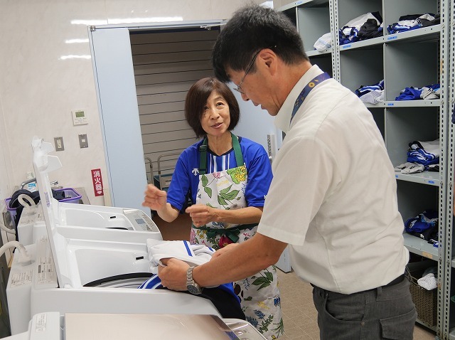 横浜スタジアムのランドリールームで最新式の洗濯機の使い勝手について話す小﨑美紀子さん（左）とハイセンスジャパンの今井俊次開発担当