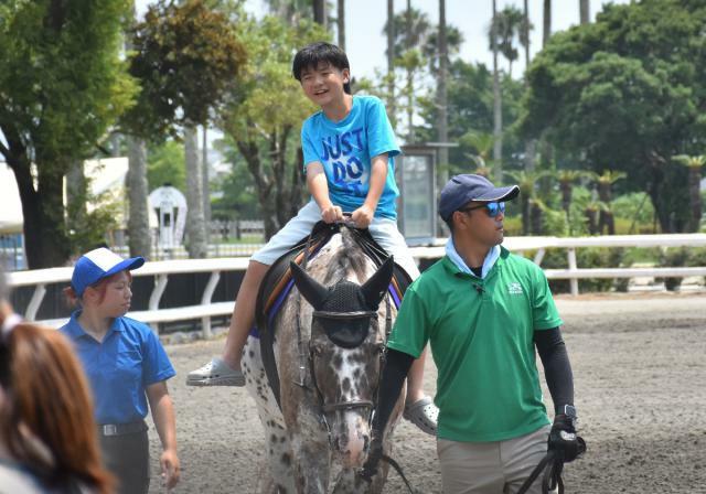 初めて馬に乗り笑顔を見せる乗馬体験参加者=12 日午前、宮崎市・ＪＲＡ宮崎育成牧場