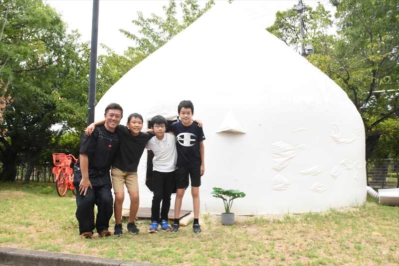 北川教授（左端）から簡易住宅を発案した経緯などを学んだ（右から）今井さん、谷川さん、佐藤さん。後ろは簡易住宅＝名古屋工業大