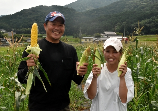 収穫したスイートコーンを持つ大上さん（左）と児玉さん