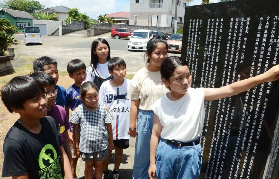 犠牲者の名前が刻まれた石碑を見つめる竹田百笑さん（右）ら岡前小学校の児童＝７月２３日、徳之島町のなごみの岬公園