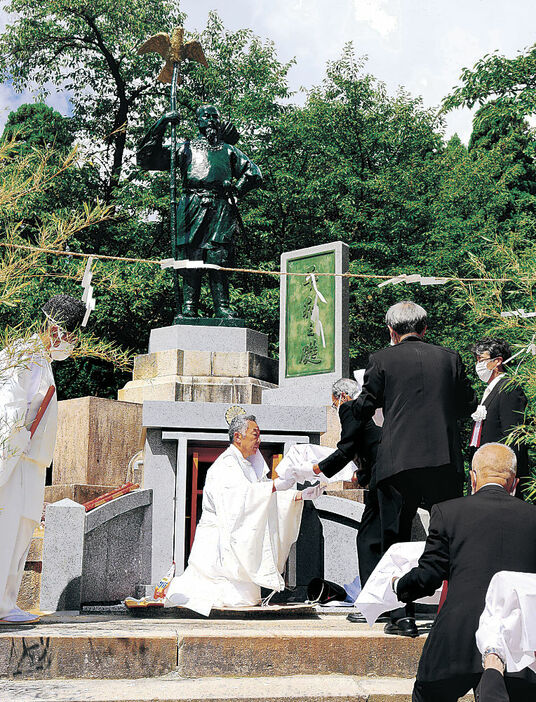 修復された神武天皇像の前で霊璽を納堂に収める保存会役員＝小矢部市の城山公園