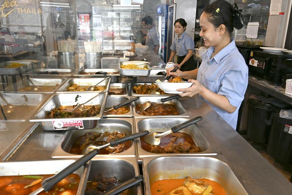 にぎわうミャンマー料理店の厨房で盛り付けをする店員＝2024年5月、タイ・バンコク（共同）