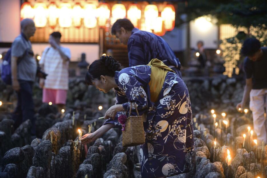 化野念仏寺で始まった「千灯供養」で、石仏にろうそくをともす参拝者＝24日夕、京都市