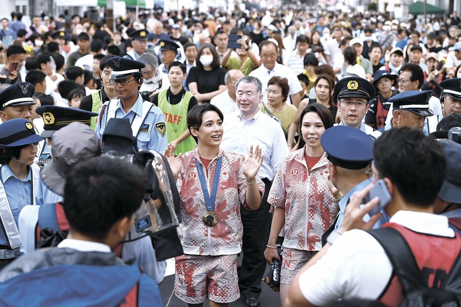 広丘駅前を歩いて地域住民らの歓声に応える出口クリスタ選手（中央）と出口ケリー選手（同右）