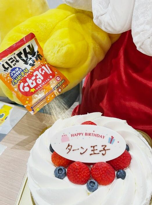 誕生日ケーキに勢いよくハッピーターンの粉をかけるターン王子　画像提供＝亀田製菓