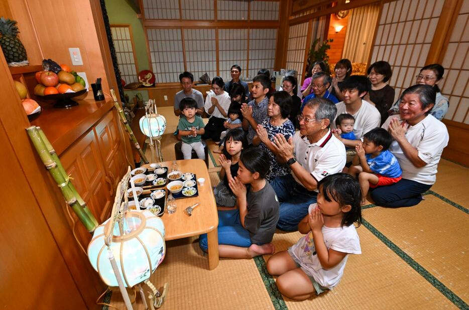 仏壇に手を合わせる高良茂光さんら家族や親族＝16日午後7時すぎ、那覇市具志（喜瀨守昭撮影）