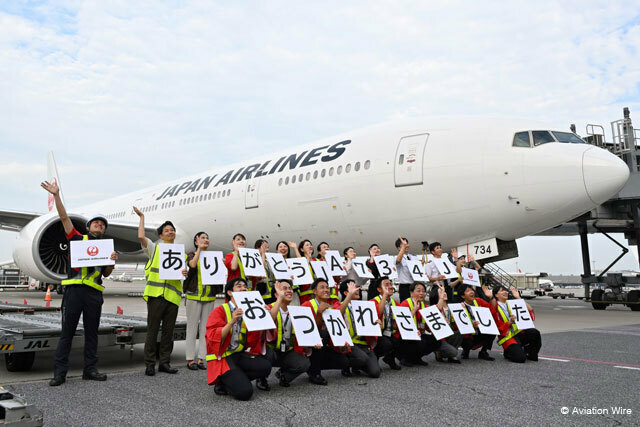 羽田空港に到着したJAL初の777-300ER退役機となるJA734Jの前でパネルを手に展望デッキに集まった人たちに手を振る社員ら。機材繰りで急きょシドニー線をもう1往復することが決まり20日が最終運航となる見通し＝24年8月19日 PHOTO: Tadayuki YOSHIKAWA/Aviation Wire