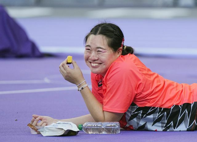 競技場で寝そべり、リラックスした様子でカステラを食べる北口榛花選手(写真:代表撮影/アフロスポーツ)