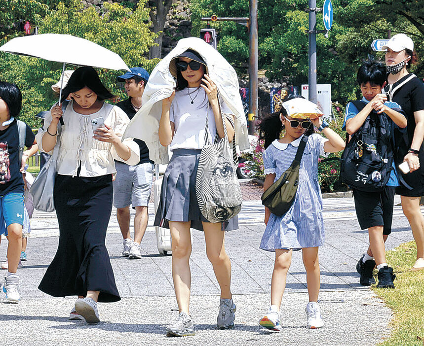 暑さをしのぎながら街中を歩く観光客＝２２日午前１０時４５分、金沢２１世紀美術館前