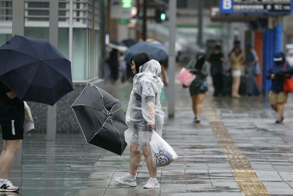 傘を風であおられる人＝29日午後3時13分、JR博多駅前