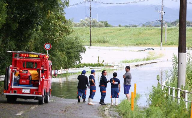 本庄川に近い宮崎市吉野では大雨で道路や田んぼなどが冠水。浸水した車両を心配そうに見つめる消防団員ら＝２９日午前１０時２９分、宮崎市吉野