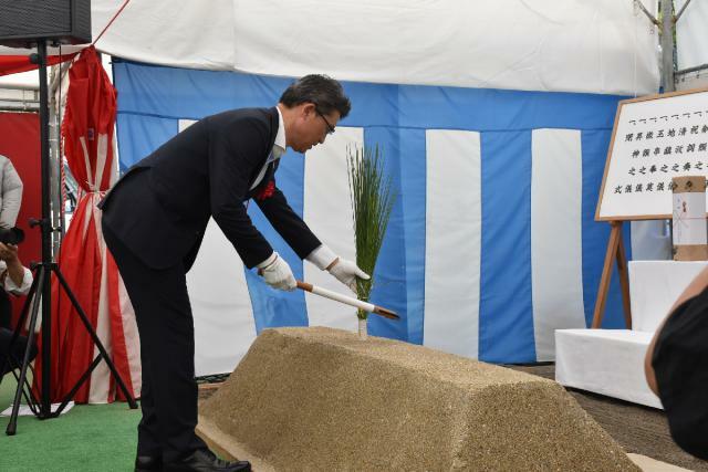 ひなた県総合運動公園庭球場の改修工事の安全祈願祭で刈り初めの儀を行う河野知事＝８日午前