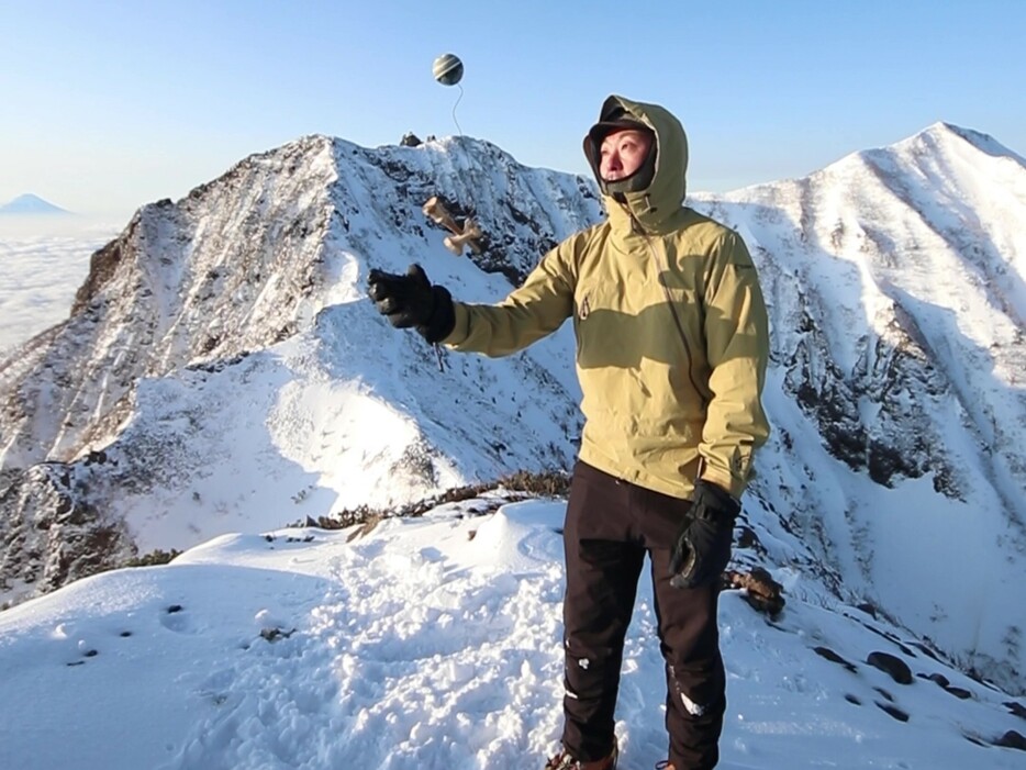 積雪した八ケ岳連峰で牛山さんが披露するけん玉（牛山さん提供）