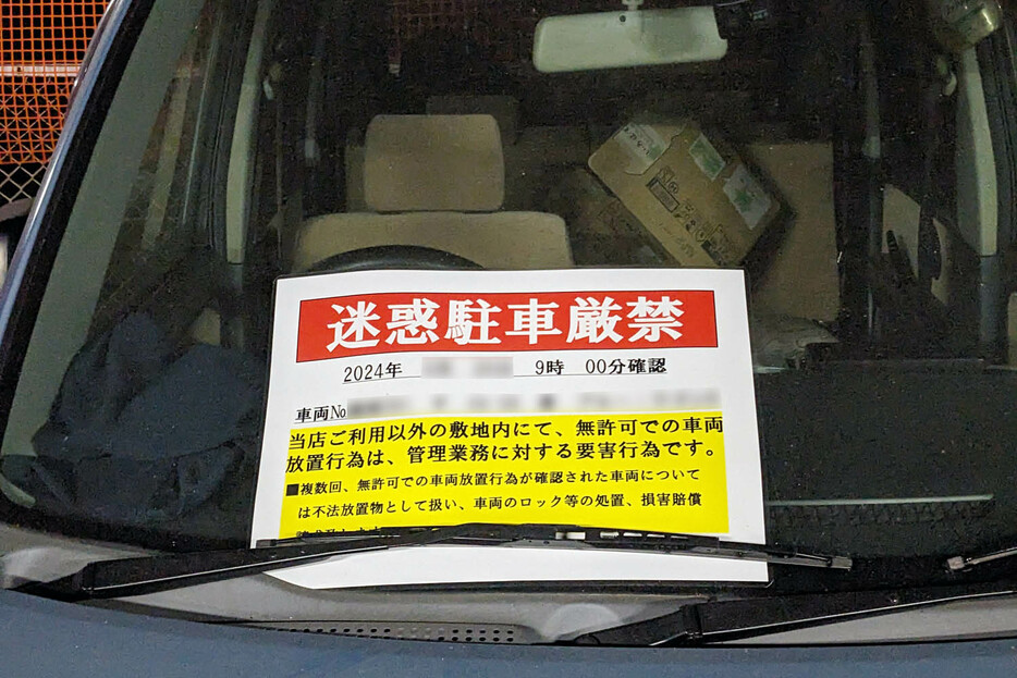 商業施設の駐車場に長期間放置された車両のワイパーに警告文が挟まれている例