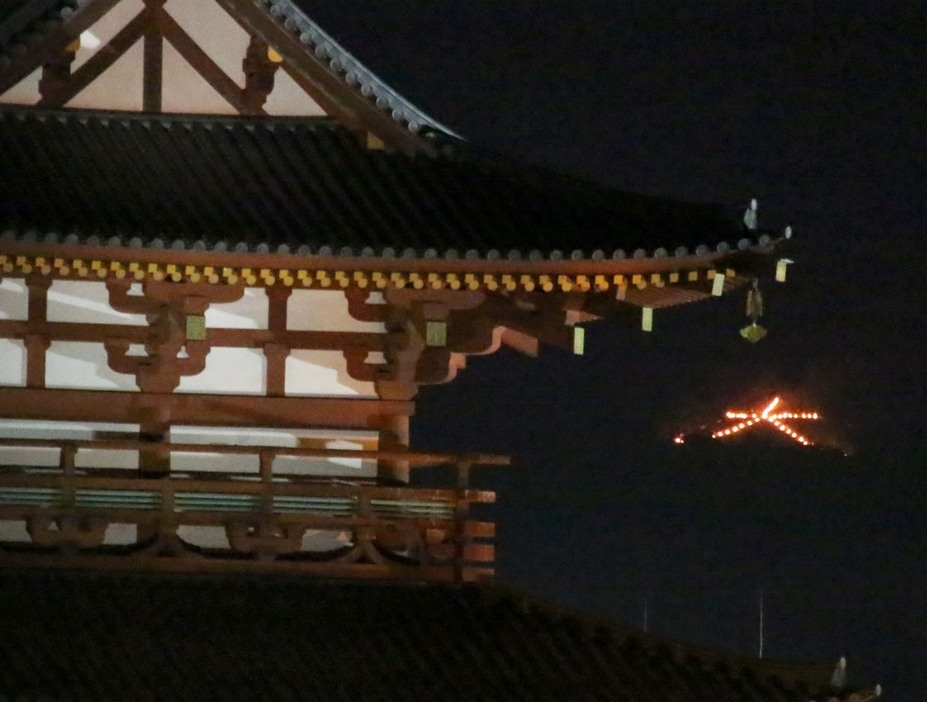 ［写真］奈良市の夜に「奈良大文字送り火」の炎が浮かびあがった。手前は平城宮跡の朱雀門＝15日午後8時10分ごろ、奈良市で