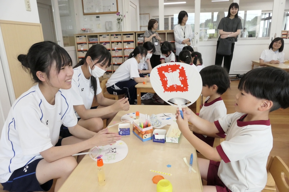 会話を弾ませながら園児とうちわを作る高校生=岡山県津山市、総社保育園で