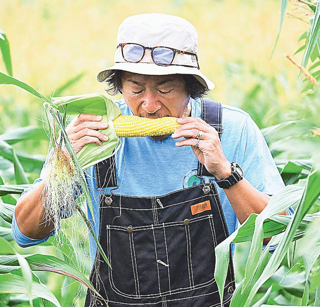 もぎたての「なおもろこし」をかじる石川さん（長野県飯綱町で）