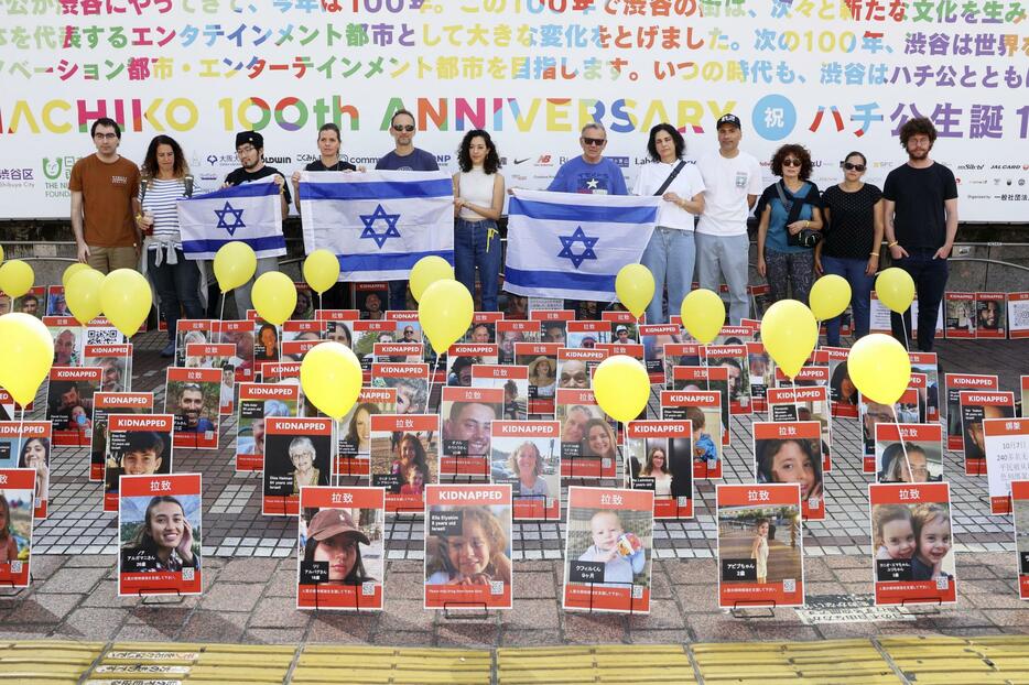 ハマスに誘拐されたとみられる人質の写真などを前に、イスラエル国旗を持って並ぶ参加者ら＝3日、東京・JR渋谷駅前