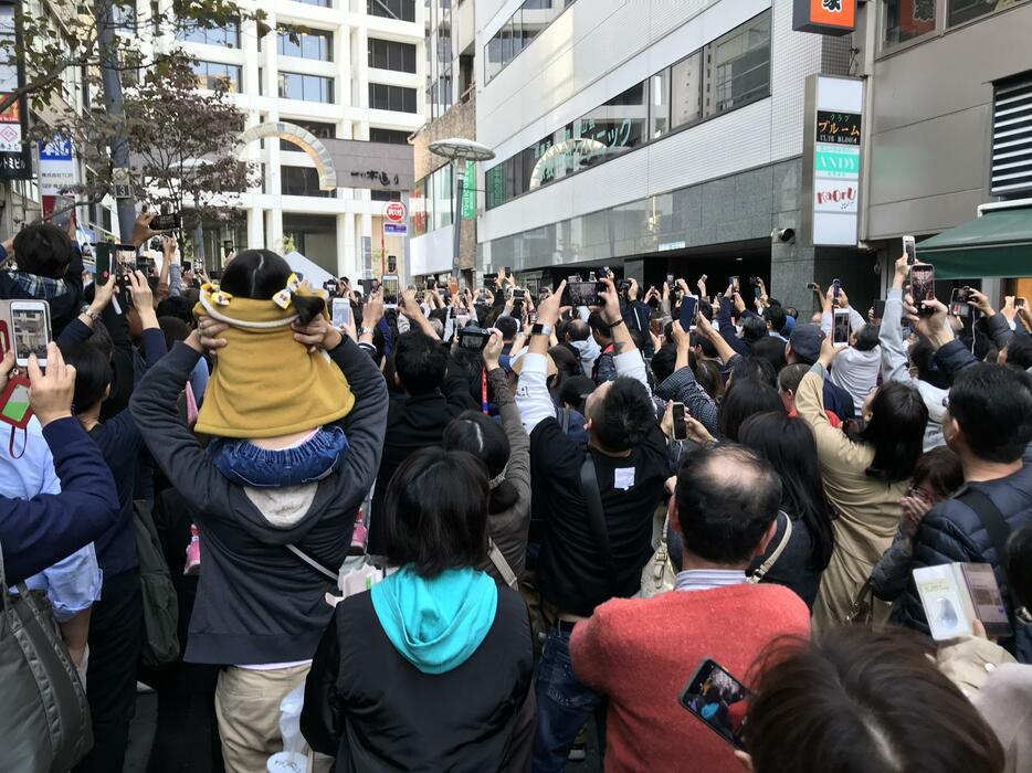 [写真]両陛下の車列が近づく気配に、一斉にスマートフォンを向ける沿道に入れなかった観覧者ら