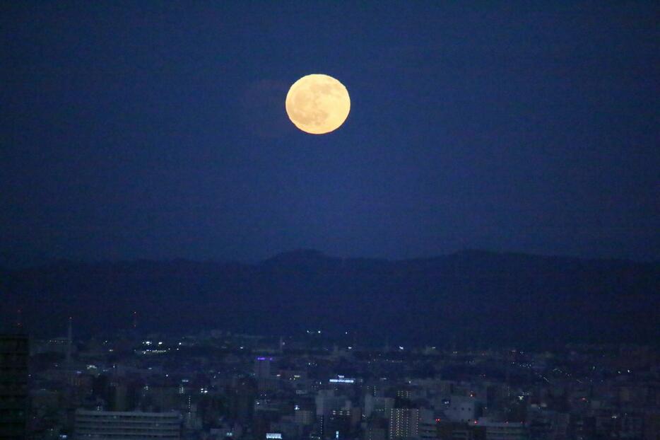 [写真]大阪駅前から北東に向かってシャッターを切ると、山の上に満月、下側に大阪市都島区周辺の夜景が写っている＝12日午後5時5分ごろ、大阪市北区から撮影