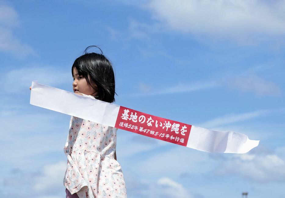 沖縄県・石垣島で行われた「平和行進」に祖母と参加し、「基地のない沖縄を」などと書かれた鉢巻を手にする子ども。日本復帰から52年を迎えた沖縄では、台湾有事を念頭に防衛力強化が続けられている＝15日午後