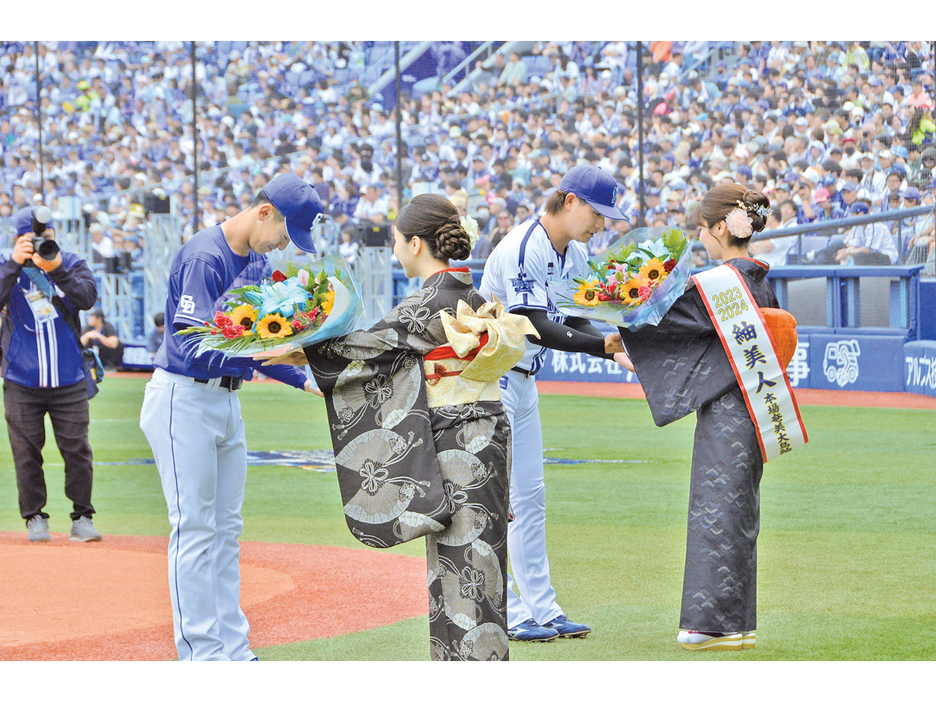 試合前のセレモニーで、選手代表に花束を手渡す紬美人の金子きよらさん（右）と奄美唄者の辻美里さん＝19日、横浜スタジアム