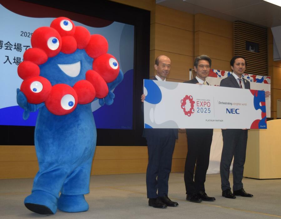 2025年日本国際博覧会協会とNECの関係者が、万博の公式キャラクター「ミャクミャク」と記念撮影した＝23日、NEC本社（東京都港区）