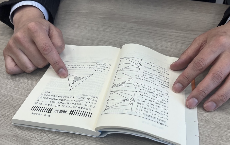 自身が小学生の時に解いた「難問」を指す坂口龍平さん。本は『解ければ天才! 算数100の難問・奇問』（中村義作著、講談社ブルーバックス）