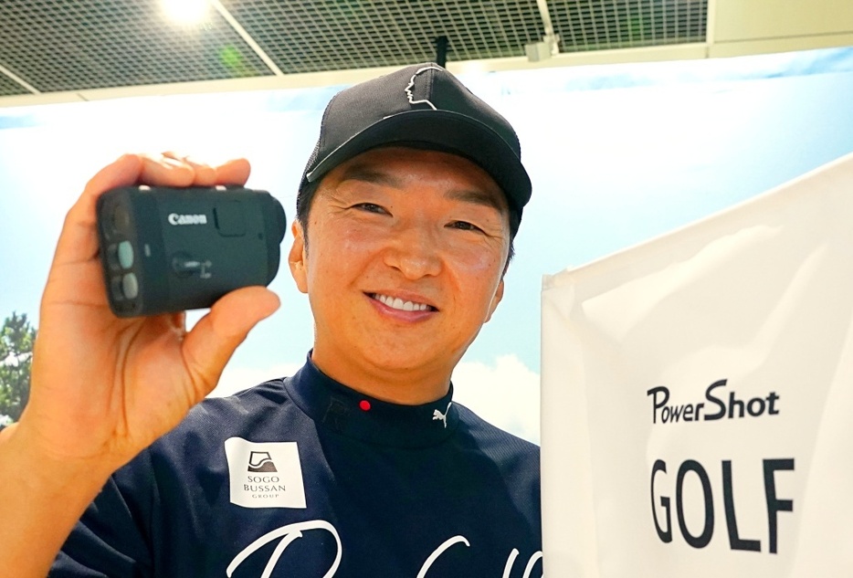 キャノンの新製品のレーザー距離計「PowerShot GOLF」を手にする進藤大典ツアープロキャディ