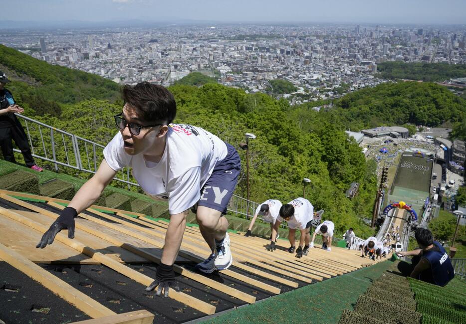 スキーのジャンプ台を着地ゾーンから頂上に向かって駆け上がる人たち＝18日午前、札幌市の大倉山ジャンプ競技場