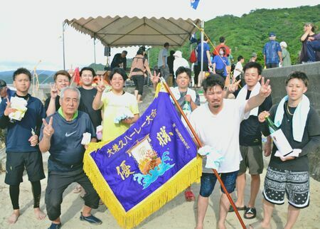 優勝旗を手にし２連覇を喜ぶ東ン門のメンバー＝１８日、大宜味村大兼久の海岸