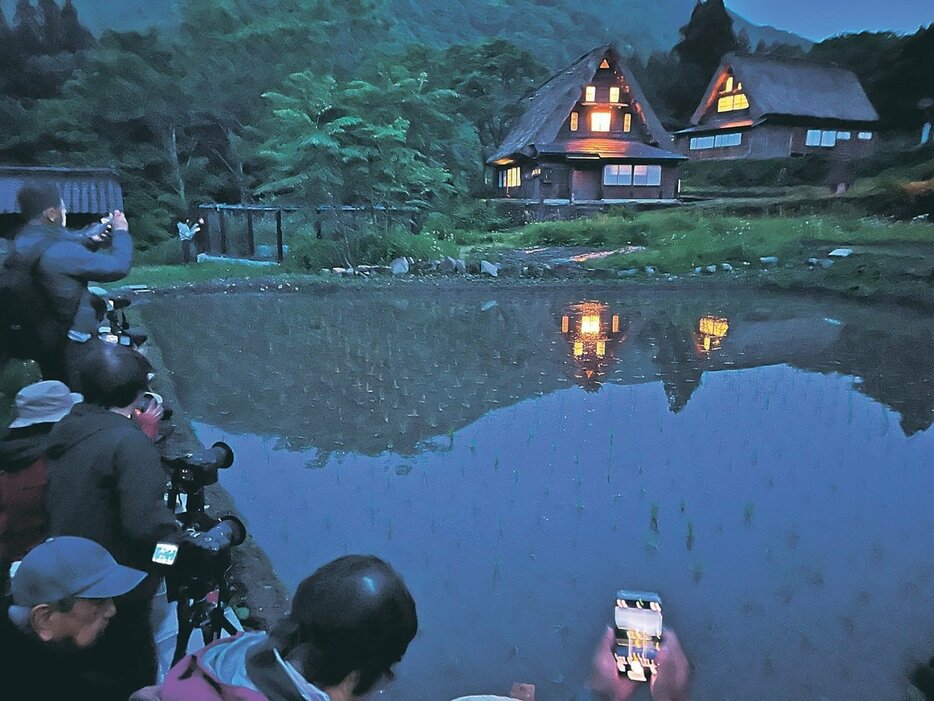 窓明かりがともされた家屋が水田に映る様子を収めようと集まったカメラマンたち＝相倉合掌造り集落